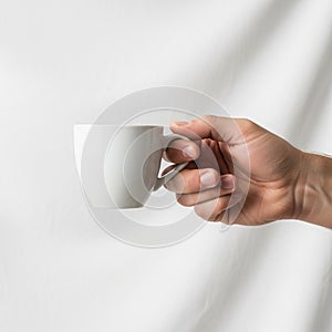 A hand is holding a small, plain white ceramic mug against a white