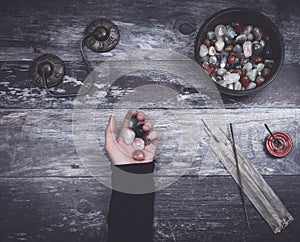 Hand holding small stones in energy healing meditation on rustic wooden table with burning incense and Tibetan prayer bells