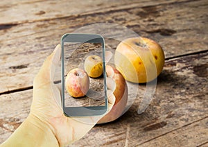 Hand holding smart phone and apple on wooden table background