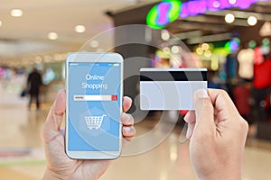 Hand holding smart phone with online shopping on screen and credit card over blurred in shopping mall background