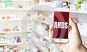 Hand holding smart phone in pharmacy drugstore. Text ARDS