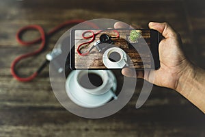 Hand holding smart phone taking photo of coffee and camera on wooden table.