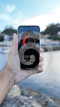 Hand holding a smartphone with a compass displayed on the screen on the background of the beach