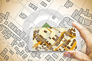 Hand holding a smartphone with an imaginary cadastral map of territory with buildings