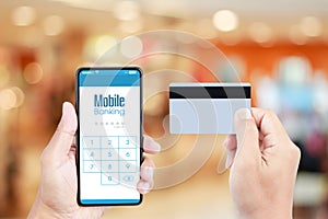 Hand holding smartphone with Mobile Banking on screen over blurred in shopping mall background