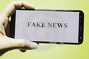 Hand holding smartphone with the phrase fake news written on the screen photo