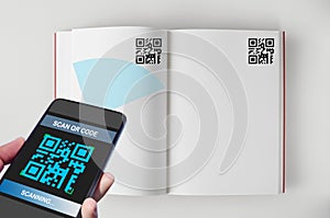 Hand holding smartphone with scanning QR code on open book screen on white background