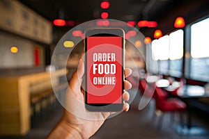Hand holding smartphone showing ORDER FOOD ONLINE app with blurred restaurant ambiance