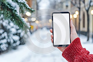 Hand holding smartphone on snowy downtown street photo