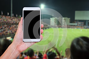 Hand holding smartphone with soccer screen in football stadium b
