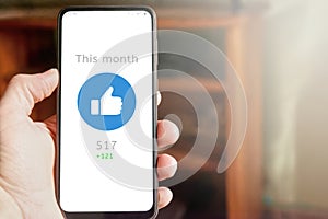 Hand holding smartphone with thumb up icon on the screen, social media report