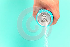 Hand holding soda can pouring a crazy amount of sugar in metaphor of sugar content of a refresh drink isolated on blue background