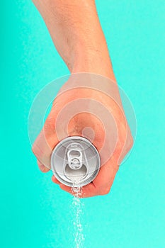 Hand holding soda can pouring a crazy amount of sugar in metaphor of sugar content of a refresh drink isolated on blue background