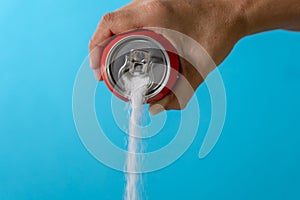 Hand holding a soda can pouring sugar