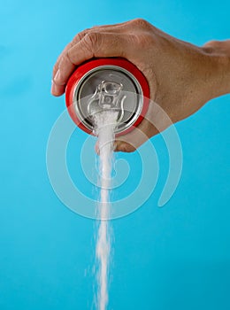 Hand holding a soda can pouring sugar