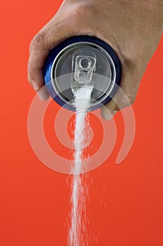 Hand holding a soda can pouring sugar