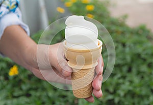 Hand holding soft white milk cream ice cream cone in summer day