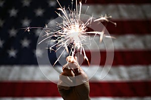 Hand holding sparkler in front of the American Flag for 4th of July celebration