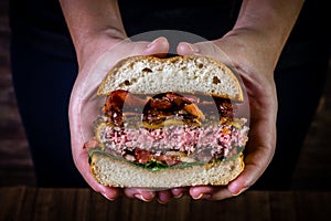 Hand holding a splited craft beef burger with cheese, bacon and rocket leafs