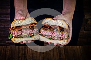 Hand holding a splited craft beef burger with cheese, bacon and rocket leafs