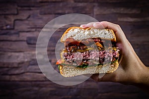 Hand holding a splited craft beef burger with cheese, bacon and rocket leafs