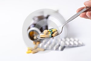 Hand holding spoon with medicine pills ,tablets and capsules with pill bottle on white background