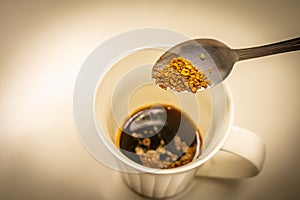 Hand holding a spoon to scoop coffee into a glass