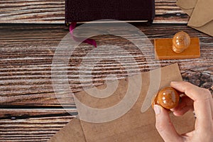 Hand holding stamp seal on ancient blank letter with bible book and old envelopes on rustic background, top view