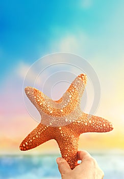 Hand holding starfish with tropical summer beach island, relaxing vacation summer blue sea concept.