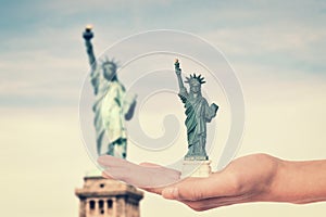 Hand holding a Statue of Liberty souvenir toy, real Statue of Liberty in the background