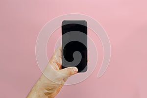 hand holding stylish black phone with empty screen on pink background, flat lay. space for text. modern instagram blogging.