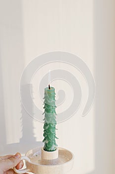 Hand holding stylish christmas tree candle on sunny white background in room. Holiday advent. Merry Christmas! Modern handmade