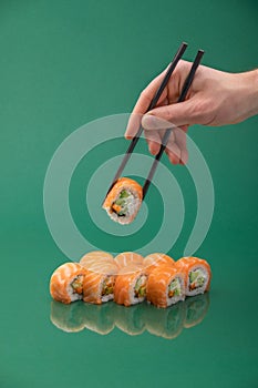 Hand holding sushi roll with chopsticks on green background. set of rolls