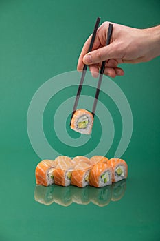 Hand holding sushi roll with chopsticks on green background. set of rolls