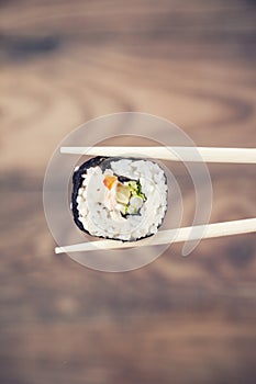 Hand holding sushi roll using chopsticks
