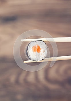 Hand holding sushi roll using chopsticks