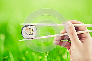 Hand holding sushi roll using chopsticks