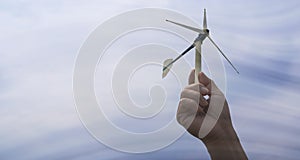 Hand holding a sustainable green energy wind turbine. The wind is moving through