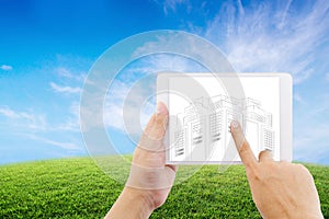 Hand holding tablet of businessman with drawing sketches of construction project on nature background.