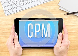 Hand holding tablet with CPM Cost per mille word on wood tabl