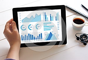 Hand holding tablet with graphs and charts elements on screen