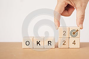 hand hold target icon with OKR dark brown text on wooden cube blocks with hand arrange 2024 for photo