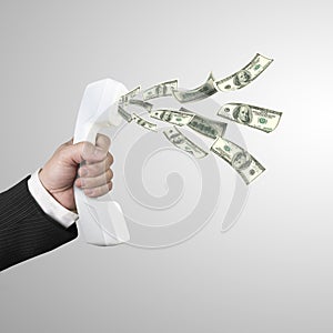 Hand holding telephone handset with money spraying out