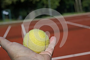 Hand holding the tennis ball above outdoor court
