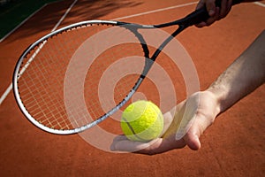 Hand holding tennis racket and ball on court