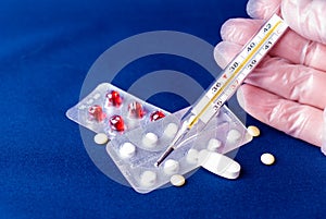 Hand holding thermometer and pill and medical equipment background.