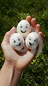 Hand holding three eggs with funny faces, promoting healthy eating