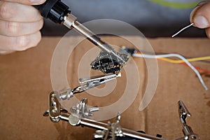 The hand holding the tin, a soldering iron solder the chip in place. a man solders a wire to a microcircuit