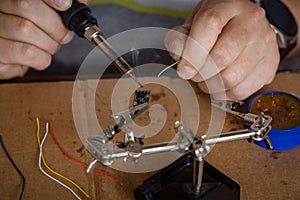 The hand holding the tin, a soldering iron solder the chip in place. a man solders a wire to a microcircuit