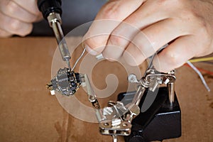 The hand holding the tin, a soldering iron solder the chip in place. a man solders a wire to a microcircuit